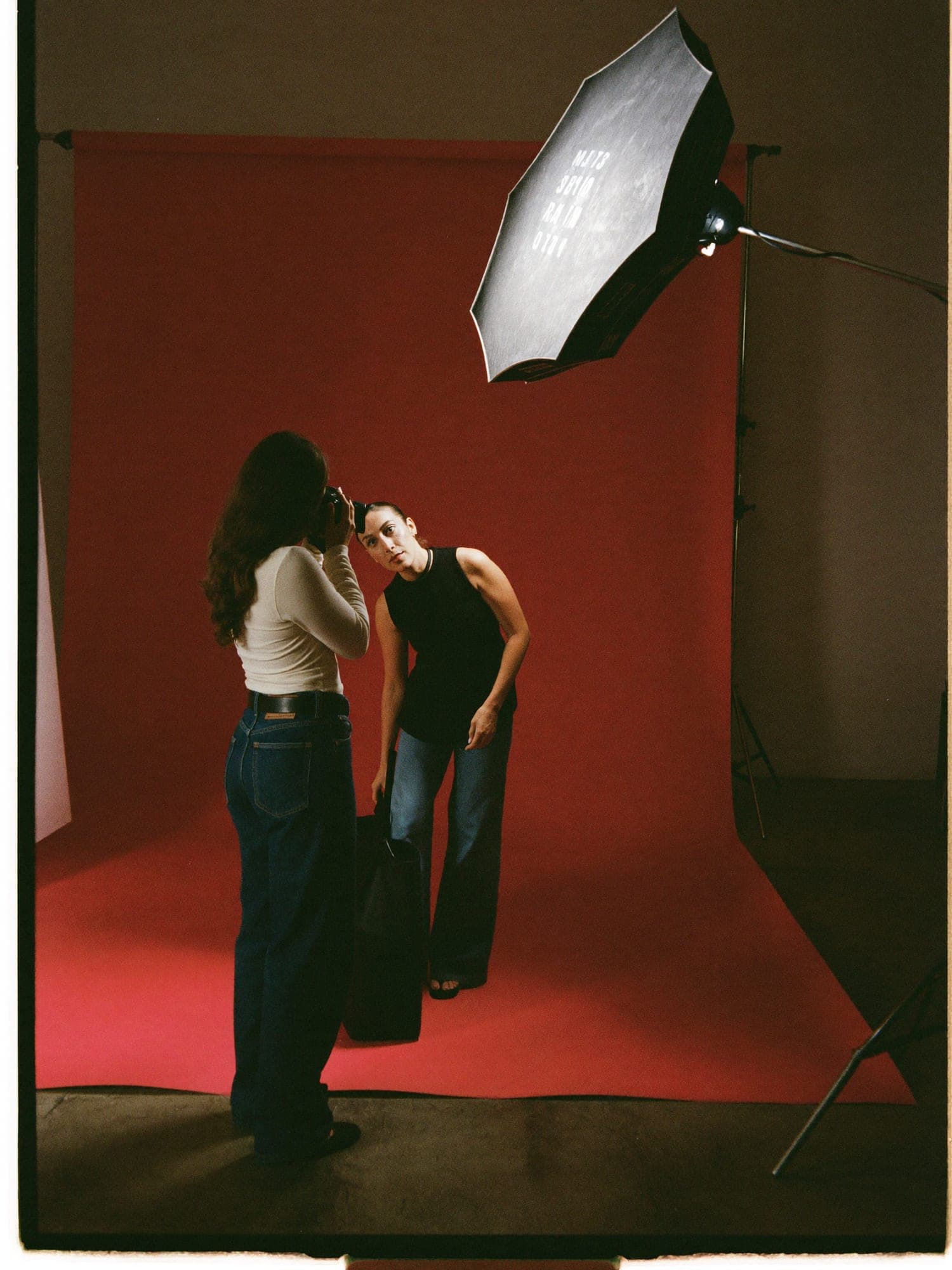 Detrás de cámaras: dos fotógrafas ajustan una softbox frente a un fondo rojo.